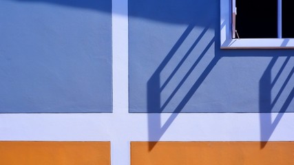 Sunlight and shadow on surface of white wooden window with blue and orange painted wall decoration background, exterior architecture concept