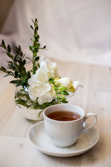 Obraz na płótnie Canvas cup of tea on a saucer and a white freesia flower