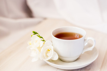 cup of tea on a saucer and a white freesia flower