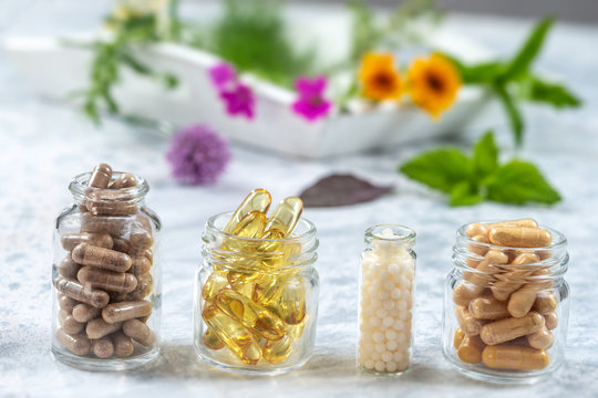Herbal supplements and vitamins on wooden tray , decorated with colorfull medicinal flowers and herbs blurry wooden background