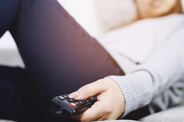 close up Television remote control in casual young female hands pointing to tv set and turning it on or off. select channel watching tv sleep on sofa at home in the living room relax.