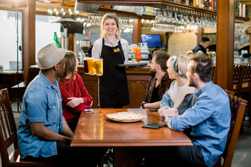 Portrait of smiling young diverse friends in indoors restaurant and smiling waitress with drinks and beer.
