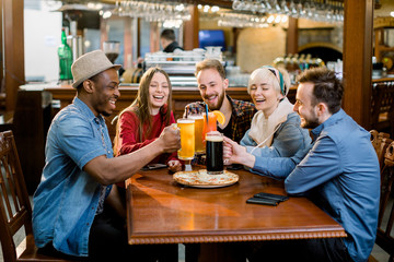 Happy multiethnic friends eating pizza, food together in cafe, laughing at joke, funny news, having fun together at meeting, excited colleagues sharing meal at lunch, hanging out together