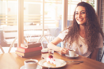 Beautiful smiling woman drinking coffee at cafe. Portrait of young woman in a cafeteria drinking hot cappuccino. Pretty woman with cup of coffee.