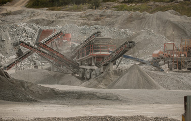 Cement production factory on mining quarry. Conveyor belt of heavy machinery loads stones and gravel. Industrial background with working gravel crusher