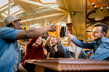 Five friends drinking beer and juice, eating pizza at cafe, diverse people laughing tell jokes having fun in public place, multiracial friendship free time concept