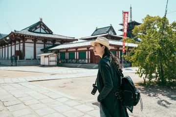 Asian woman travel alone in japan on summer vacation. girl backpacker walking in beautiful temple during hot sunny day with blue sky. female tourist carry camera while visiting in shitennoji shrine