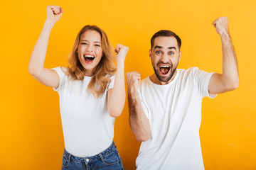 Portrait of surprised content couple man and woman in basic t-shirts rejoicing and clenching fists