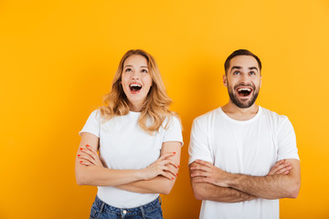 Portrait of excited young couple man and woman in basic t-shirts wondering and looking upward with arms crossed