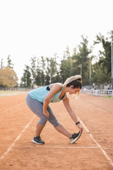 Sporty woman stretching on stadium track