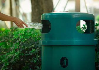 People hand throwing empty water bottle in recycle bin at park. Green plastic recycle bin. Man discard bottle in trash bin. Waste management. Plastic bottle garbage. Reduce and reuse plastic concept.