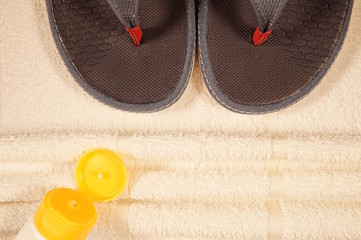 background of a draped towel, a pair of thongs/flip-flops and sun cream. Beach border summer...