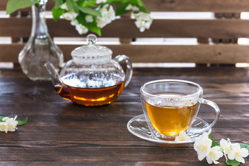 Cup of jasmine tea and transparent tea pot on the wooden table. Spring tea party. Copy space