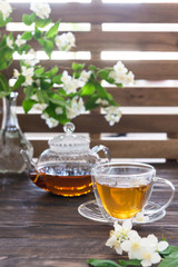 Cup of green tea with jasmine flowers and tea pot on wooden background. Copy space