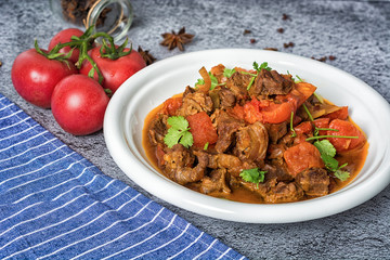 Veal stewed with vegetables in tomato sauce on a black concrete or stone background.