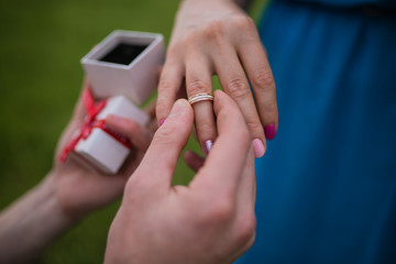 A man holds a wedding ring in front of a surprised happy girl with a bouquet of flowers, covering his mouth with his hand. Romantic photo