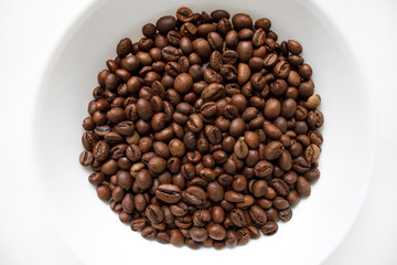 coffee beans brown closeup with blurred background in white plate on white isolated background