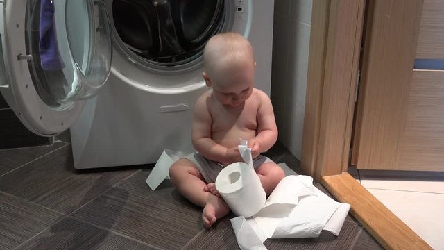 Caucasian child boy play with toilet paper rolls in bathroom