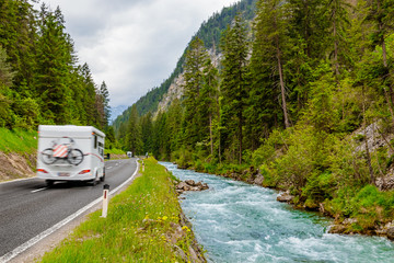 Camper van with attached bicycle driving through the European Alps on a rainy day.