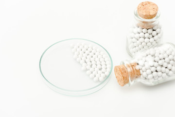 selective focus of round small pills in glass petri dish near bottles with wooden corks isolated on white