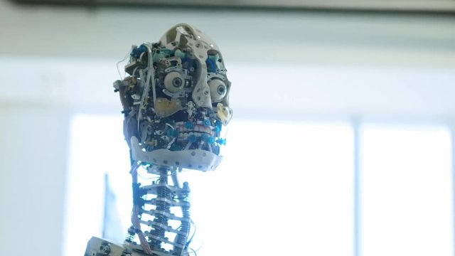 Futuristic humanoid female robot is idle. Concept of future. The head of a humanoid android humanoid robot. The robot turns his head, blinks his eyes. Android skull