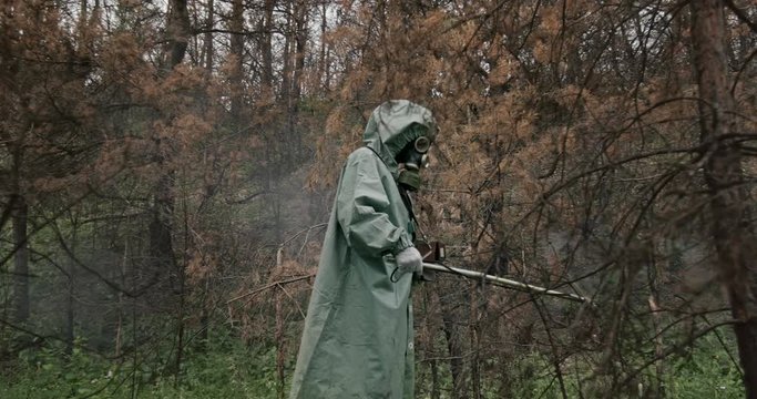 The dosimeter, a man in a gas mask and special chemical protection, green cloak measures the dose of radiation contamination by a military dosimeter.