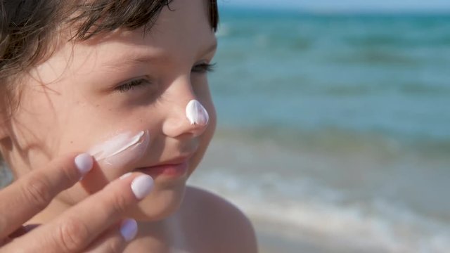 The face of a child in sunscreen. A mother's hand applies sunscreen to her little daughter's face. Protect your child with sunscreen.