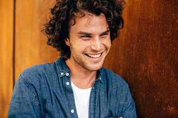 Closeup portrait of handsome young man with curly hair, smiling and looking aside, standing at...
