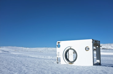 Сlothes washer frame reminding part of airplane fuselage left in the middle of snow desert with snowmobile trail behind it
