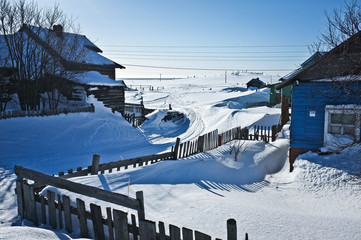 Nearly abandoned fishers settlement on Kola Peninsula; twisty road with snowmobile trail placed between blue, green and grey wooden houses