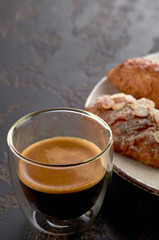 Small cup of espresso with foam and almond croissants on a plate. Vertical.