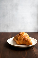  Сroissant on white plate on grey back on wooden back