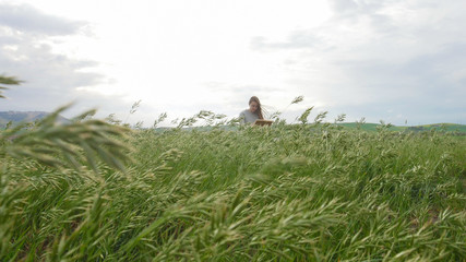 A young woman sits on the green field with high grass and drawing on a canvas