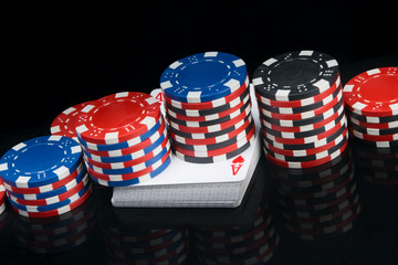 on a black background with a reflection, on a deck of cards, there are pyramids of colored chips for playing poker