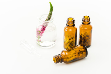 pink veronica flower in glass bottle near pills on white