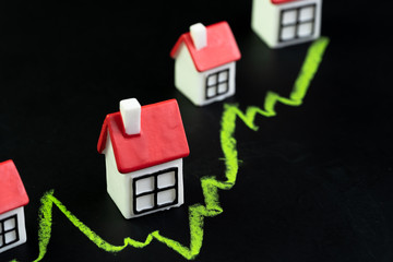 House, property or real estate market price go up or rising concept, small miniature house with green line graph going up on black chalkboard