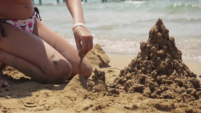 Girl playing on the beach building sand castle. Slow motion.