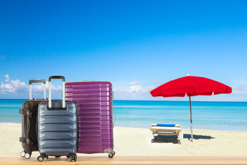 Modern suitcases baggage for travelling or business trip on wooden floor against amazing beach ocean coast background with sun lounger under red umbrella. Travel or vacation concept.