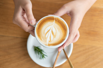 Woman hand holding a white coffee mug.  Coffee is a latte. table on the wooden table in vintage style, taken from the top view, see the froth of milk foam.