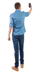 Fototapeta premium Back view of man who makes selfie with a smartphone.