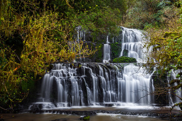 Fototapeta na wymiar Purakaunui falls waterfall located in a serene forest. The Purakaunui Falls are a cascading three-tiered waterfall on the Purakaunui River, in The Catlins region of the South Island, New Zealand.