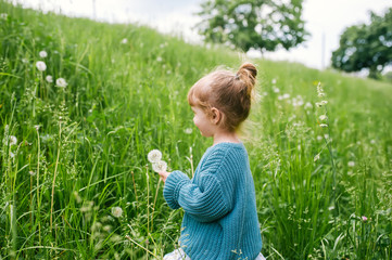 Fototapeta premium Little girl with dandelion on green grass background.