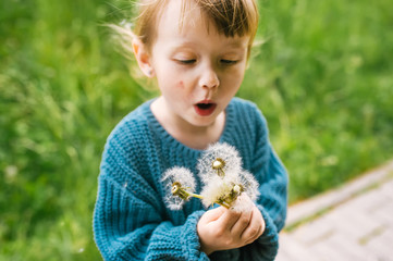Baby girl making wish and blowing dandelion nature background.