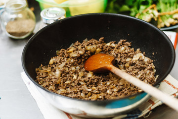 The chef roasts the mince in a deep pan. Ready stuffing with onions in a bowl on the background of spices and greens.