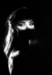 Beautiful girl model with red lips make up and naked shoulders in the shade, with a lit silhouette and a strip of light illuminating her eyes. Conceptual, art, fashionable design. Black and white
