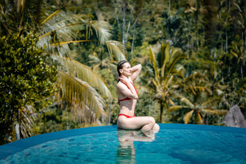 Fototapeta premium Woman in tropical vacation sitting in the water of pool