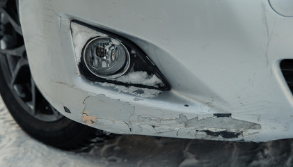 A broken bumper after a car crash, scratches and cracked bumper on a white car. winter snow.