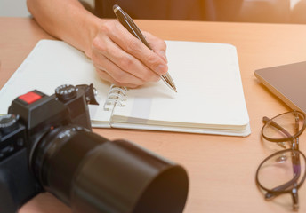 Close up shot of hand that are writing pen on notebook. working time with laptop, camera and glasses.