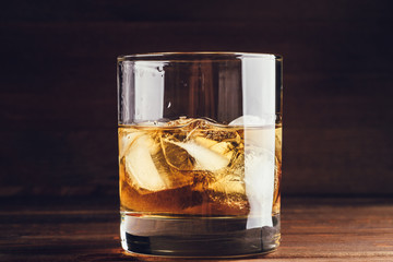 Whiskey glass with ice cubes on wooden background