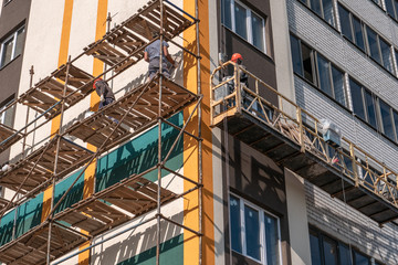 Construction workers on scaffolding on new building wall in construction site